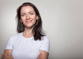 Portrait of a confident woman smiling with arms crossed, wearing a white t-shirt on a gray background.